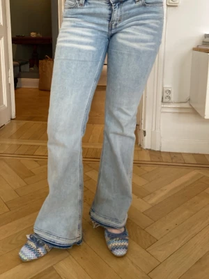Ljusblå bootcut jeans - Säljer ett par ljusblå bootcut jeans med slitningar framtill. Jeansen har låg midja och är tillverkade i denim med lätt stretch. Perfekta för en avslappnad och trendig look.