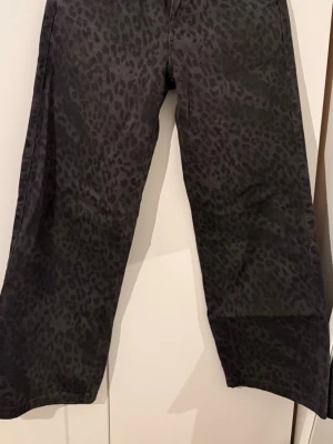 Svarta jeans med leopardmönster low waist - Low waist. Säljer ett par svarta jeans med coolt leopardmönster. Byxorna har raka ben och en klassisk femficksmodell. Perfekta för dig som vill sticka ut lite extra med ett djurmönster i garderoben.