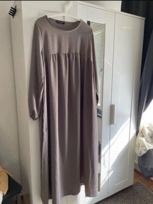 Taupe Långklänning/Abaya Onesize - Långklänning/Abaya i taupe med rund halsringning och långa ärmar. Nyskick. Längden är 140 cm. 