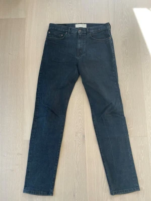 Mörkblå raka jeans Jeanerica - Snygga mörkblå jeans med rak passform och klassisk femficksdesign. Jeansen har hög midja och stängs med knapp och dragkedja. Perfekta för en clean och stilren look.