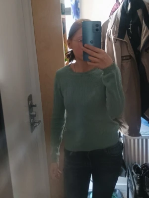 Grön stickad tröja med rund hals - Mysig stickad tröja i ljusgrönt med rund halsringning och långa ärmar. Tröjan har en enkel, klassisk design utan synliga mönster eller detaljer. Perfekt att matcha med jeans för en avslappnad look.