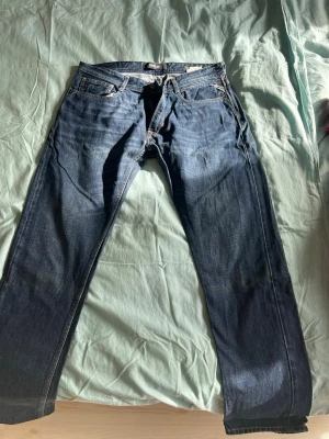 Blå raka jeans från Replay - Snygga blå jeans från Replay med klassisk femficksdesign och raka ben. Jeansen har subtila slitningar och en läderpatch med Replay-logga bak i midjan. Perfekta för en avslappnad och trendig look.