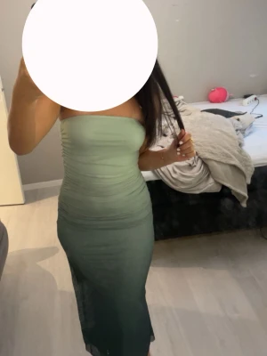 Grön axelbandslös långklänning - Snygg axelbandslös långklänning i ljusgrön till mörkgrön toning. Klänningen har en tight passform och är figurnära med lätt rynkade detaljer. Perfekt för dig som vill ha en stilren och trendig look. Använd en gång