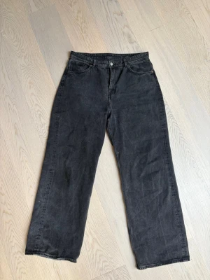 Svarta raka jeans med hög midja - Säljer ett par svarta jeans med rak passform och hög midja. Jeansen har klassisk femficksdesign och stängs med knapp och dragkedja. Materialet är denim i bomull. Perfekta för en avslappnad och trendig look.