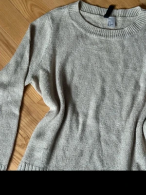 Beige stickad tröja med rund hals - Mysig stickad tröja med rund halsringning och långa ärmar. Tröjan har breda ribbstickade muddar vid ärmslut och nederkant. Perfekt för lager på lager och enkel att matcha till olika outfits.