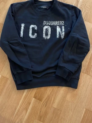 Svart sweatshirt från Dsquared2 ICON - Cool svart sweatshirt från Dsquared2 med stor vit 'ICON'-text framtill och rund hals. Tröjan har ribbade muddar vid ärmslut och nederkant. Tillverkad i mjukt material som känns skönt mot huden. Perfekt för dig som gillar streetwear och vill sticka ut.