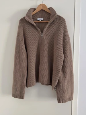 & Other Stories Stickad tröja i ull och bomull blandning - Storlek M - Säljer en beige/brun stickad tröja från & Other Stories med halvzip och hög krage. Tröjan har avslappnad passform, breda ärmar och ribbstickad struktur. Perfekt för lager på lager och enkel att styla till olika outfits.