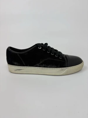 Svarta Lanvin sneakers med mockadetaljer - Stilrena svarta sneakers med ovandel i mocka och tåparti i slätt läder. Skorna har svarta snören, metallöljetter och en vit, något smutsad sula. Perfekta för en clean och urban look.