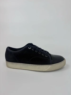 Svarta Lanvin sneakers med lackad tå - Stilrena svarta sneakers med ovandel i mocka och snygg lackad tå. Skorna har vita sulor och svarta skosnören. Perfekta för dig som gillar en clean look med en twist. Metallfärgade öljetter ger extra detalj.