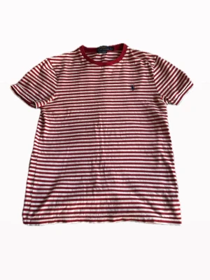 Randig t-shirt från Polo Ralph Lauren - Snygg t-shirt från Polo Ralph Lauren i rött och vitt med horisontella ränder. Klassisk rund halsringning och broderad logga på bröstet. Modellen är slim fit och passar perfekt till sommaren!