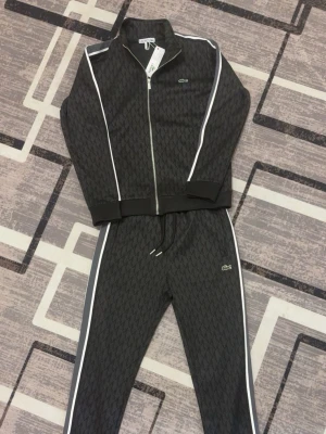 Lacoste dress - Snygga svarta mjukisbyxor från Lacoste med vitt mönster och vita ränder längs. Perfekta för en chill och sportig stil. Sitter väldigt fint.
