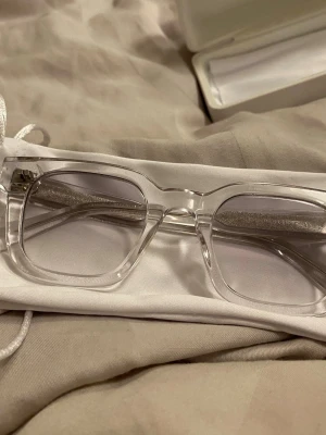 Chimi 04 vita glasögon - Säljer ett par stilrena solglasögon från Chimi med transparent båge och fyrkantig form. Glasögonen har ljusgrå tonade linser och levereras med vit förvaringspåse och etui. Perfekta för dig som vill ha en clean och modern look. Priset går att diskuteras vid snabb affär, skriv om ni har några frågor