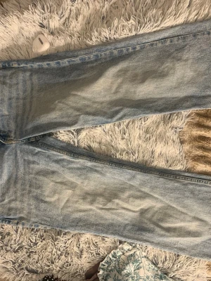 Ljusblå raka jeans - Säljer ett par ljusblå jeans med rak passform och klassisk femficksdesign. Jeansen har en tvättad look med subtila slitningar och är tillverkade i denim. Perfekta för en avslappnad och trendig stil.