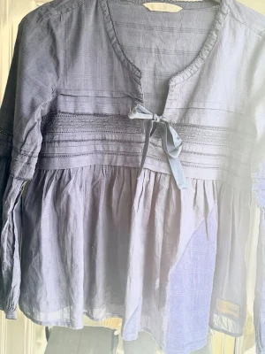 Djup blå  blus från Odd Molly - Supersöt djupblå blus från Odd Molly med lång ärm, dekorativ knytning framtill och fina broderade detaljer. Blusen har en lös passform och är tillverkad i ett tunt, vävt material med diskret rutmönster.