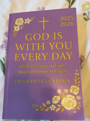 God Is With You Every Day 2025-2026 - En lila bok med guldfärgade blommor och text, 'God Is With You Every Day 2025-2026' av Valer Din Cucerdea. Innehåller 365 reflektioner om tro, hopp och inre styrka. Perfekt för dig som söker daglig inspiration och styrka.
