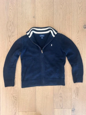 Mörkblå stickad Ralph Lauren tröja med zip och krage - En riktigt snygg marinblå Ralph Lauren tröja. Storlek Barn L/14-16 år. Använd några få gånger med sjukt bra skick. Endast 349 kr! Kontakta vid minsta fundering! 😁