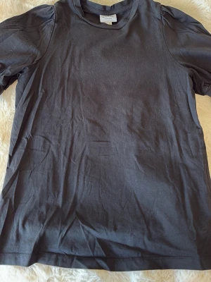 Svart topp med puffärm från Aware - Svart topp från Aware med korta puffärmar och rund halsringning. Tillverkad i mjuk bomull, perfekt för en stilren och enkel look. Klassisk passform och diskret design som funkar till många outfits. Skriv för frågor❤️