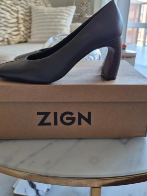 Bruna pumps med blockklack från Zign - Snygga brun/ grå  pumps från Zign med trendig fyrkantig tå och stabil blockklack 7 cm. Skorna med foder och innersula i skinn, har en stilren design som passar till många outfits. Perfekta för dig som gillar en modern och minimalistisk look.Använda en gång. Kommer med originalkartong. Köpta på Zalando.