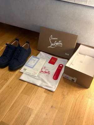 Mörkblå Christian Louboutin sneakers - Snygga mörkblå sneakers från Christian Louboutin i mocka med klassisk röd sula och diskret logga. Skorna har lågt skaft, svarta skosnören och en stilren design som passar perfekt till streetwear eller en mer dressad look.