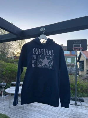 Mörkblå Original hoodie - Mörkblå hoodie med vit text och stort stjärntryck på bröstet. Trycket har en vintage-look med texten 'Original Fit Est. 2024'. Hoodien har huva och en stor magficka framtill. Perfekt för en avslappnad och cool stil.