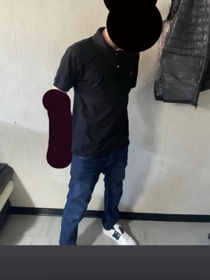 Svart pikétröja från Ralph Lauren - Klassisk svart pikétröja från Ralph Lauren med röd broderad logga på bröstet. Tröjan har korta ärmar, krage och knappar framtill. Perfekt för en stilren och avslappnad look. Pris kan diskuteras 