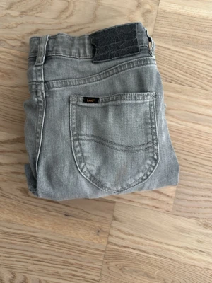 Grå jeans från Lee Daren - Snygga grå jeans från Lee, modell Daren. Klassisk femficksdesign med raka ben och normal midja. Jeansen är tillverkade i mjukt denimtyg och har en svart patch bak i midjan. Perfekta för en avslappnad och trendig look.