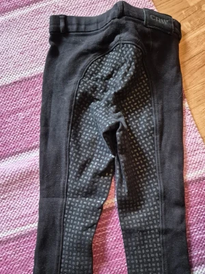 Svarta ridleggings från CRW - Säljer ett par svarta ridleggings från CRW med helskoning i silikon för extra grepp. Leggingsen har en bekväm midja och stretchigt material som passar perfekt för ridning. Snyggt prickigt mönster på helskoningen ger en sportig look.