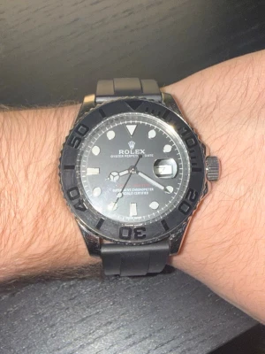 Rolx klocka - Klocka med svart urtavla och svart vridbar bezel. Klockan har datumfönster och tydliga indexmarkeringar. Armbandet är i svart gummi vilket ger en sportig känsla. Perfekt accessoar för dig som gillar exklusiva detaljer.