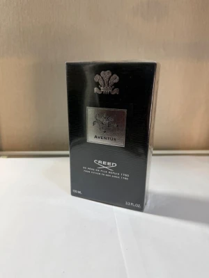 Creed Aventus Eau de Parfum 100ml - Creed Aventus Eau de Parfum i elegant svart förpackning med silverdetaljer. Flaskan rymmer 100 ml och är känd för sin lyxiga och ikoniska doft. Perfekt för dig som vill ha en exklusiv parfym med stilren design.