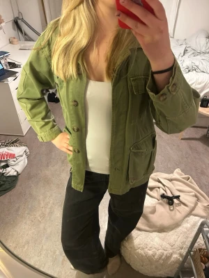 Grön jacka från Zara😎 - Snygg grön overshirt i bomull med klassisk krage och stora utanpåliggande fickor framtill. Jackan har knäppning med knappar och avslappnad passform, perfekt att slänga på över en t-shirt. Enkel och stilren design utan synligt märke. Jag är 178cm och bär storlek s från en Zaras gamla kollektion trf🌟😻en liten fläck på ryggen men inte tänkt mycket på det när jag använt den, håret hamnar över i bästa fall!