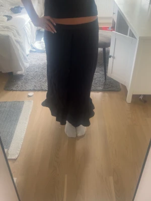 Svart långkjol med volangkant - Snygg svart långkjol med volangkant nertill. Kjolen har en klassisk och stilren design med en lätt utsvängd form. Perfekt till sommaren!