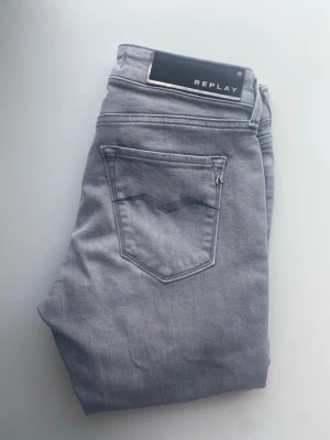 Grå jeans från Replay - Snygga grå jeans från Replay med klassisk femficksdesign och diskret logga på bakfickan. Jeansen har en slim fit/skinny-modell och är tillverkade i mjukt denimtyg med stretch för extra komfort. Perfekta för en trendig och avslappnad stil.