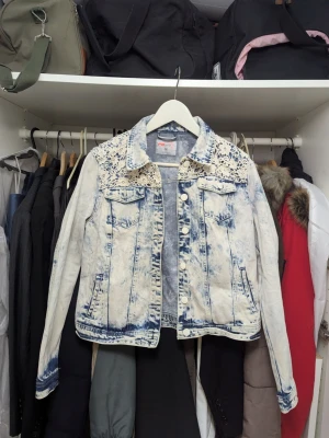 Acid wash jeansjacka med spetsdetaljer - Snygg acid wash jeansjacka från FB Sister i ljusblått och vitt. Jackan har spetsdetaljer på axlarna, klassisk krage, två bröstfickor med lock och knappar framtill. Perfekt för dig som vill sticka ut med en unik denimlook.
