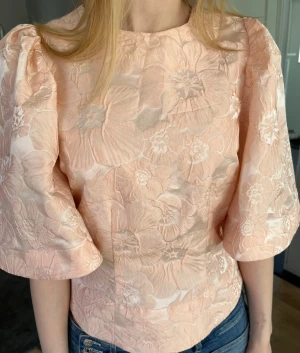 Persikofärgad blus med puffärm - Ny med prislapp! Superfin persikofärgad blus med stora puffärmar och vackert blommigt mönster i jacquardtyg.