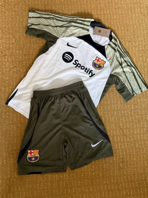 Fc Barcelona  träningssätt - Snygga svarta träningsshorts och T shirt  från Nike med FC Barcelona-logga på ena benet och vit swoosh på andra. Shortsen har elastisk midja och är perfekta för fotboll eller träning. Lätta och bekväma med sportig look.