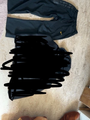 Svart Nike tech NOCTA  byxor - Svart loungewear set från Nike NOCTA med matchande hoodie och byxor. Setet har gula detaljer, inklusive NOCTA- och Nike-loggor. Hoodien har dragkedja och fickor med svarta dragkedjor. Byxorna har resår i midjan och en liten gul Nike-logga. Byxorna står det st M fast passar som S och samma sak med Nike tech koftan så står det st S men passar Xs. Pris går diskutera 