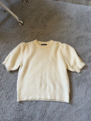 Krämvit puffärm stickad tröja Gina Tricot - Säljer en krämvit stickad tröja från Gina Tricot med puffärmar och rund halsringning. Tröjan har kortare ärmar och ribbade muddar vid hals, ärmslut och nederkant. Perfekt för dig som gillar en enkel men trendig look.