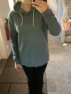 Blå hoodie med vita snören - Säljer en enkel och stilren blå hoodie med huva och vita dragsnören. Hoodien har en avslappnad passform och är tillverkad i mjukt material, perfekt för chill dagar. Långa ärmar och ribbade muddar vid ärmslut och nederkant. I höger armhåla finns ett hål, se bild.
