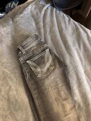 Grå bootcut jeans med kontrastsömmar - Snygga grå jeans med bootcut passform och vita kontrastsömmar. Bakfickan har ett coolt broderat mönster som sticker ut. Klassisk femficksmodell i denim, perfekt för dig som gillar en avslappnad men trendig stil.
