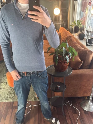 Blå halvzip-tröja Tommy Hilfiger - Snygg blå långärmad tröja från Tommy Hilfiger med halvzip och liten logga på bröstet. Tröjan har ribbade muddar och krage, perfekt för en stilren och avslappnad look. Materialet känns mjukt och bekvämt.