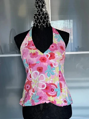 Blommig halterneck linnetopp - Färgglad halterneck linnetopp med blommigt mönster i rosa, rött, turkost och vitt. Toppen har omlott-skärning och är perfekt för varma dagar. Tunt och lätt material med en feminin och somrig vibe.