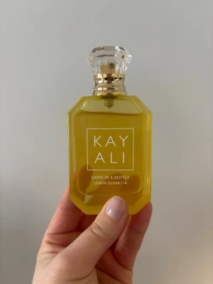 Kayali Capri In A Bottle Lemon Sugar  - Kayali Capri In A Bottle Lemon Sugar 14 är en parfym i en snygg, gul, åttakantig glasflaska med kristalliknande kork och gulddetaljer. Doften har noter av citron, socker, fresia, hallon, vanilj och mysk. Perfekt för dig som gillar fräscha och söta dofter. Säljes för att den använd för sällan men god och sprudlande doft.