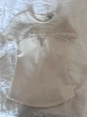 Vit spetsblus med kort ärm - Söt vit blus med spetsdetaljer över axlar och bröst. Blusen har rund halsringning, korta ärmar och en liten v-ringad öppning framtill. Materialet är strukturerat och ger en elegant känsla. Säljer då den blivit för liten💕 pris kan diskuteras 