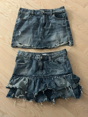 Två jeanskjolar med slitna detaljer - Två coola jeanskjolar i blå denim. Ena kjolen är rak med slitna kanter och råa detaljer, den andra har volanger och fransig nederkant för en edgy look. Båda har klassiska fickor och bälteshällor. Perfekta för dig som gillar streetstyle.