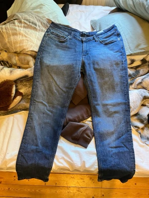 Blå jeans från Jack and Jones - Snygga blå jeans med klassisk rak passform och fem fickor. Jeansen har en mörk tvätt och subtila slitningar framtill. De har bälteshällor och knappgylf. Perfekta för en avslappnad och trendig look.
