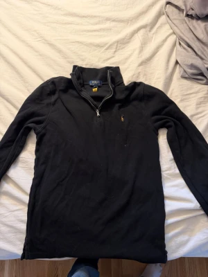Svart halvzip från Polo Ralph Lauren - Svart långärmad tröja från Polo Ralph Lauren med halv dragkedja och ståkrage. Klassisk broderad logga på bröstet. Perfekt för lager-på-lager och enkel att matcha med jeans eller chinos. Sitter som en Small! 