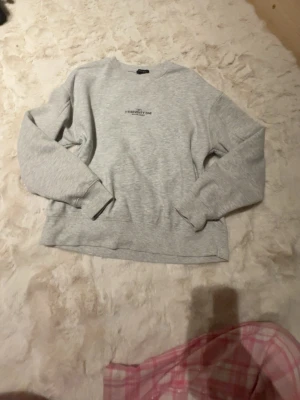 Grå sweatshirt från Amisu XS - Mysig grå sweatshirt från Amisu i storlek XS. Tröjan har rund hals, diskret tryck framtill och långa ärmar med ribbade muddar. Perfekt för chill dagar eller när du vill ha en enkel och clean look.