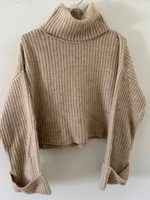 Beige stickad polotröja - Mysig beige ribbstickad polotröja med långa vida ärmar. Tröjan har hög polokrage.