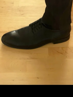 Svarta klassiska loafers i läder, använda 3 timmar. - Stilrena svarta loafers i äkta läder med slät tå och låg klack. Skorna har en minimalistisk design utan synliga detaljer och passar perfekt till en dressad look. Klassisk form med rundad tå och diskreta sömmar längs sidorna.