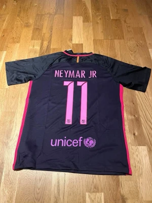 FC Barcelona Neymar Jr matchtröja - Säljer en svart och rosa FC Barcelona matchtröja från Nike med Neymar Jr och nummer 11 på ryggen. Tröjan har klubbmärke, Qatar Airways-tryck på bröstet och Unicef-logga bak. Korta ärmar och sportig passform, perfekt för fotbollsträning eller support.